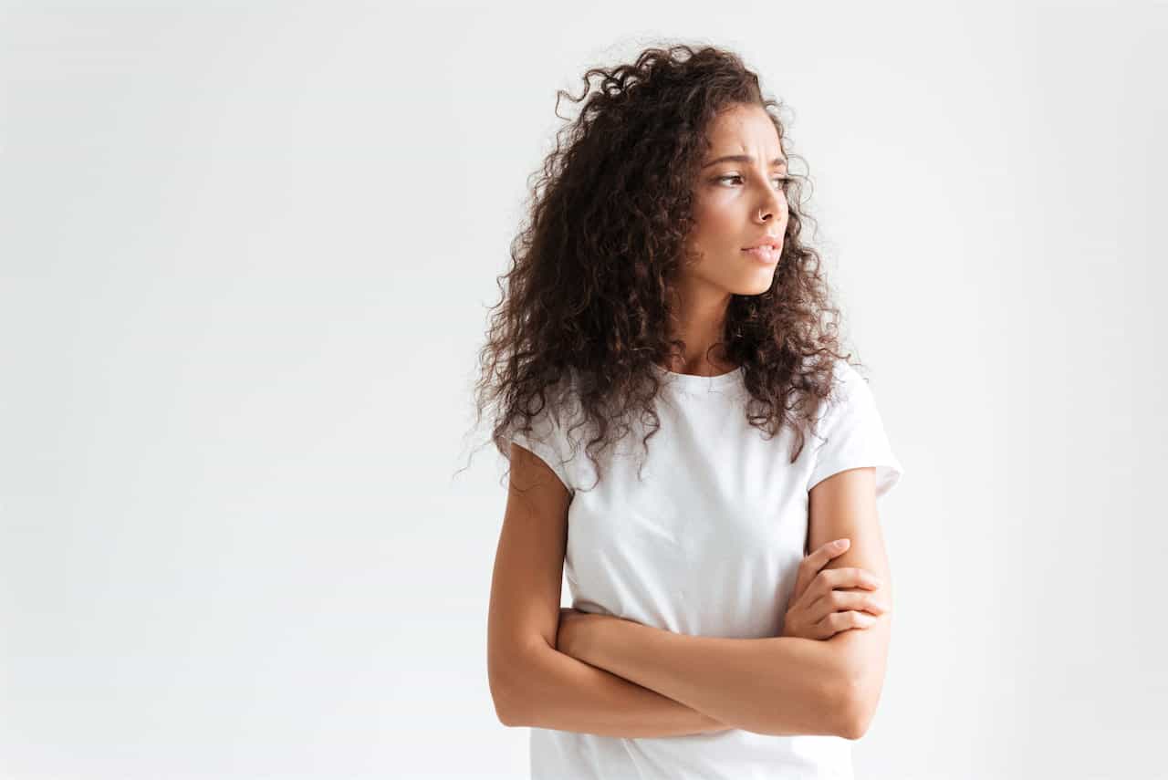 Upset young woman with curly hair standing with arms folded