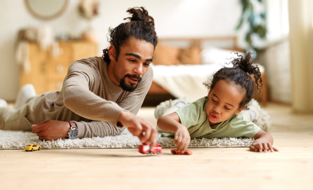 Happy african american family father and child son laughing while playing toys together at home
